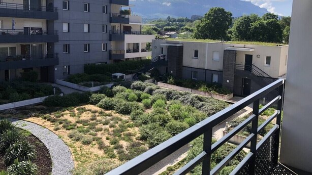 A modern apartment complex with multiple balconies, a courtyard with greenery, and a mountain view in the background. - Appartement 46m² 1 chambre, parking, proche du lac (Aix-les-Bains)