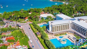 Et resort med en stor swimmingpool, en strand og et bjergrigt landskab i baggrunden.