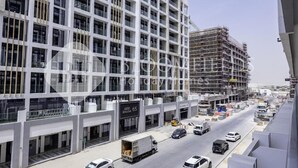 A modern building with a grid-like facade, a covered parking area, and a construction site in the background.