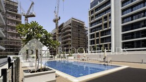 A rooftop swimming pool with a wooden deck, surrounded by modern buildings and construction cranes.