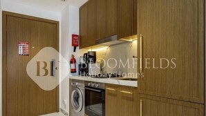 A modern kitchen with wooden cabinets, a built-in oven, a washing machine, and a coffee maker.