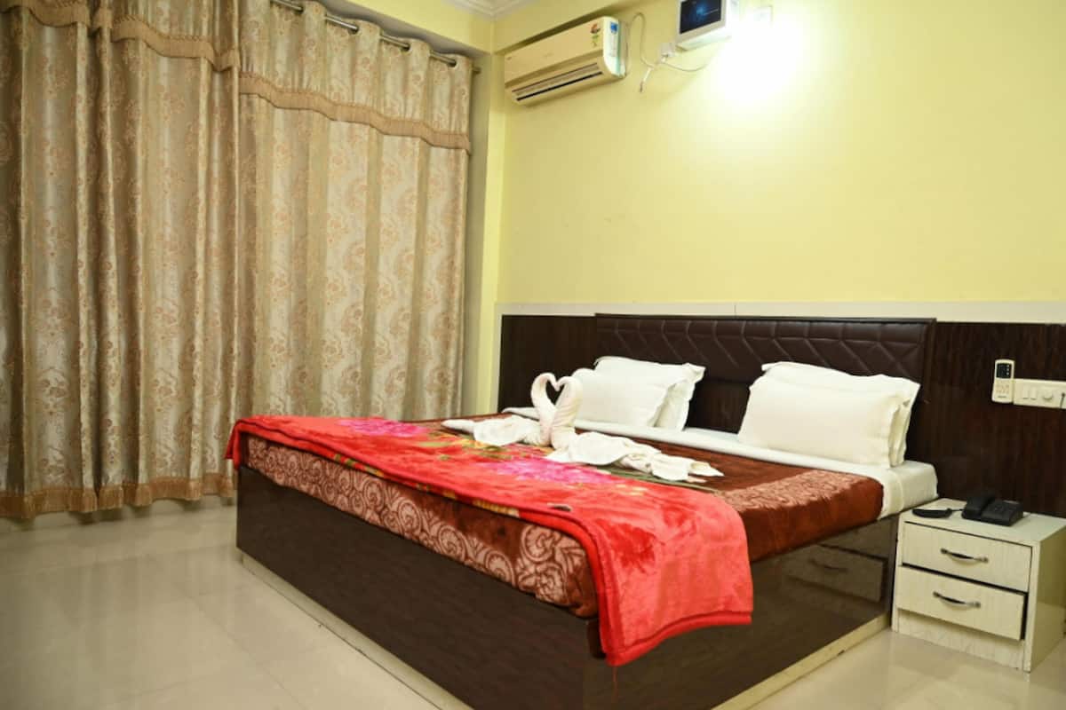 A hotel room with a bed, a nightstand, an air conditioning unit, and a curtain.