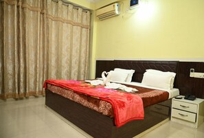 A hotel room with a bed, a nightstand, an air conditioning unit, and a curtain. - Hotel Home Inn Bodhgaya (Bodh Gaya)