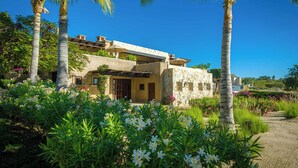 Une maison moderne à la façade en pierre, entourée d’une végétation luxuriante et de palmiers.