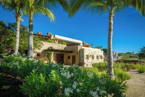 A modern house with a stone facade, surrounded by lush greenery and palm trees. - 6BR Puerto Los Cabos Retreat | Infinity Pool, Beach Club, Walkable Beaches & Near San Jose (San Jose del Cabol)