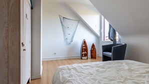 Ett sovrum med ett sluttande tak, en säng, en stol och två dekorativa träföremål.
