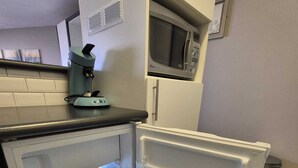 Une cuisine compacte équipée d’un four à micro-ondes encastré, d’une machine à café et d’un réfrigérateur avec des étagères transparentes.