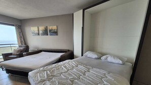 Une chambre d’hôtel avec un grand lit, un lit plus petit, un canapé et une vue sur la mer par la fenêtre.