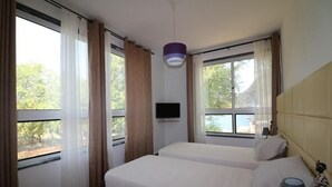 A hotel room with two beds, a TV, and large windows with curtains. - Vista Mar (Tarrafal)