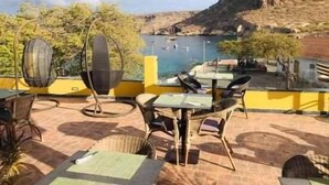 An outdoor seating area with tables and chairs, overlooking a body of water and a mountainous landscape. - Vista Mar (Tarrafal)
