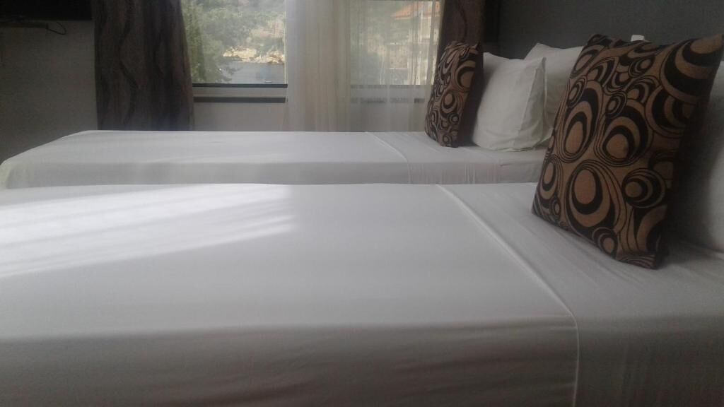 A hotel room with two beds, each with white bedding and patterned pillows.