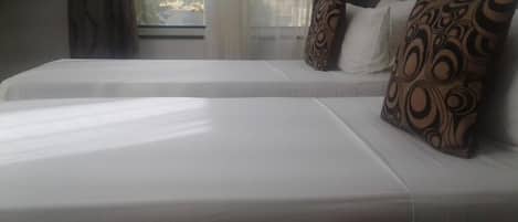 A hotel room with two beds, each with white bedding and patterned pillows.