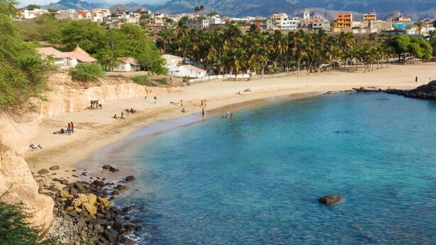 A coastal town with a sandy beach, clear blue waters, and a backdrop of mountains. - Vista Mar (Tarrafal)