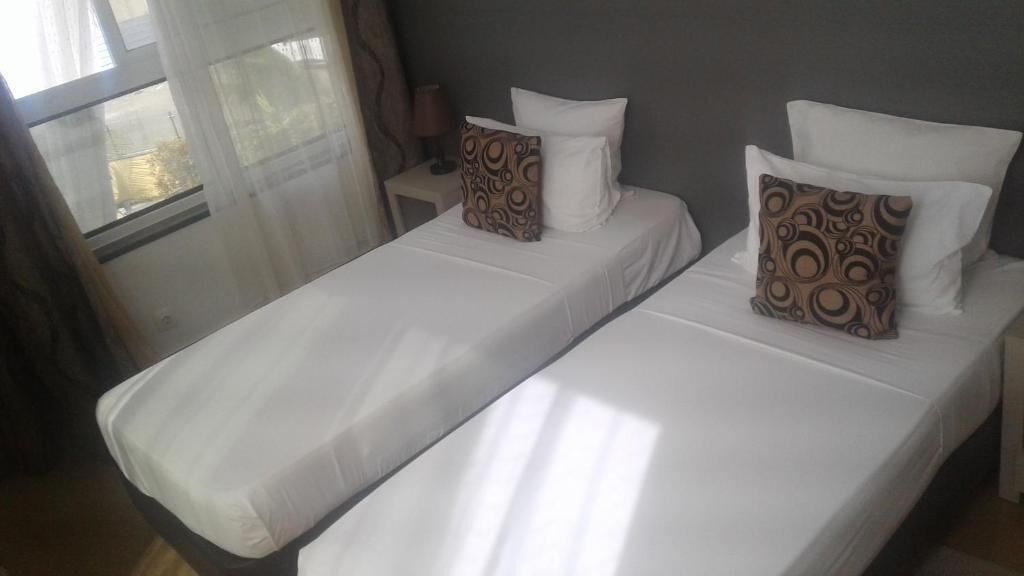 A hotel room with two single beds, each with white linens and patterned pillows.