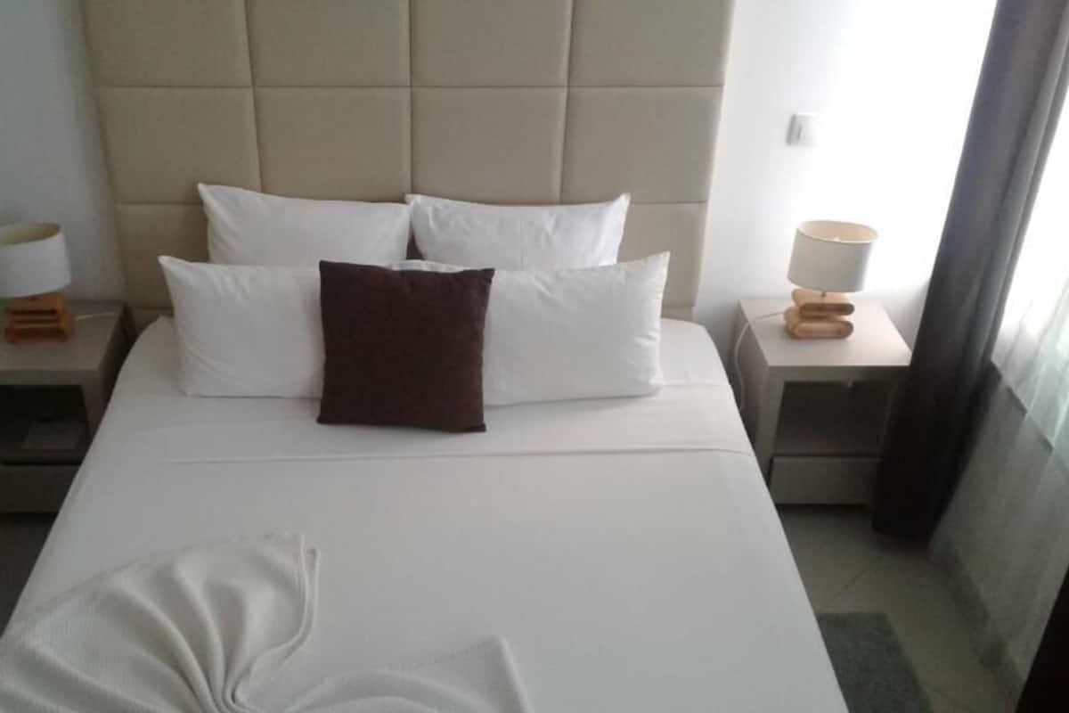 Una habitación de hotel con una cama grande, dos mesitas de noche y un cabecero.
