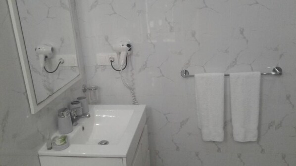 A bathroom with a white sink, a mirror, a hairdryer, and two towels hanging on a towel rack.