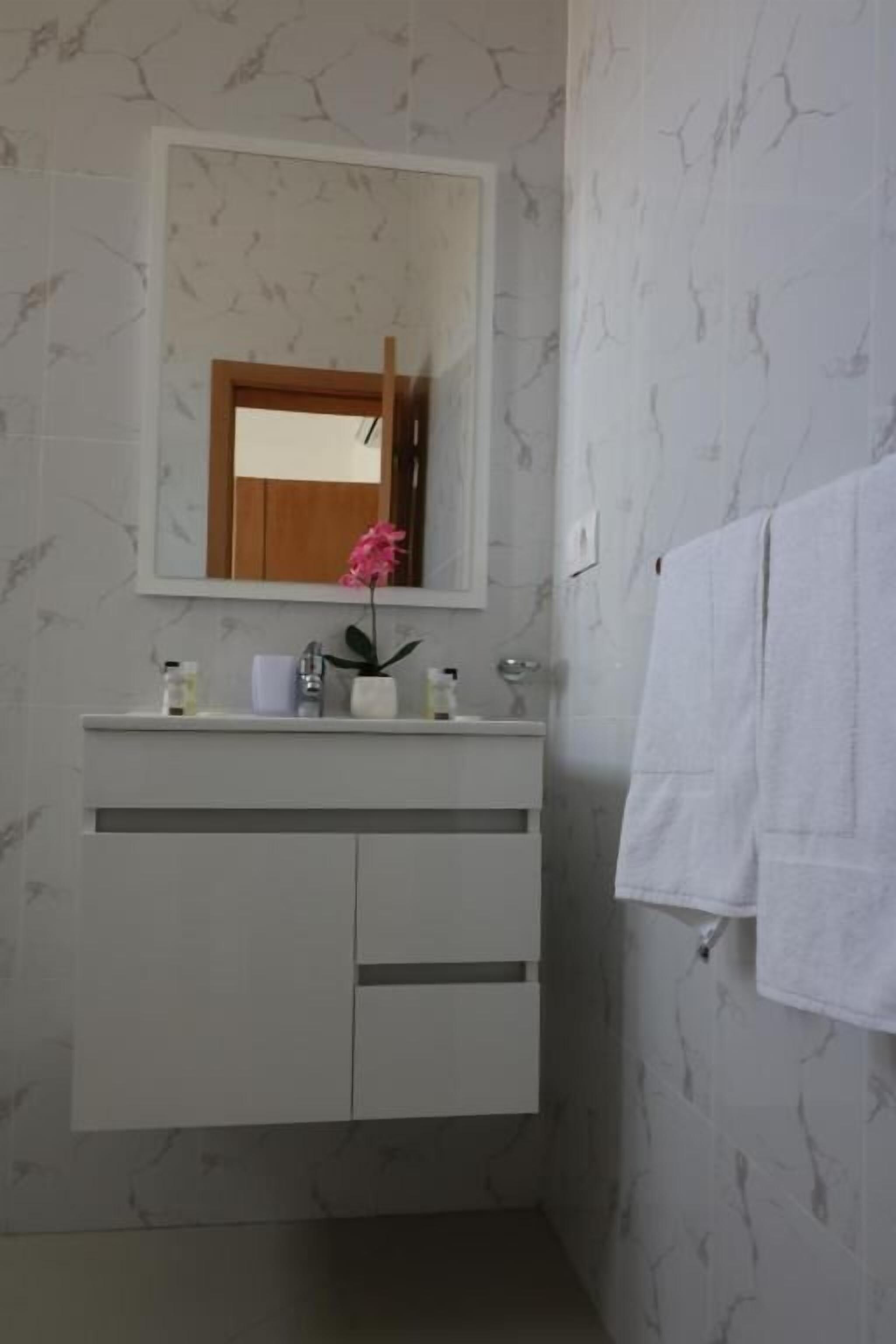 A bathroom with a marble-patterned wall, a white vanity with a mirror above it, and a towel hanging on the wall.