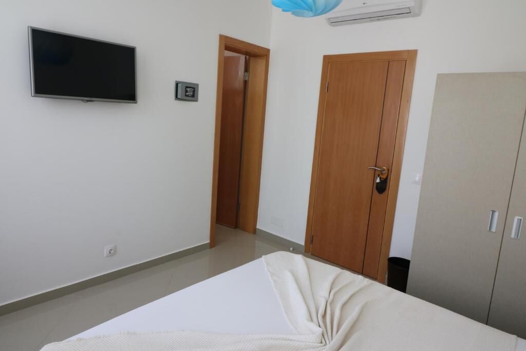 Un dormitorio con cama, televisor en la pared, armario y una puerta.