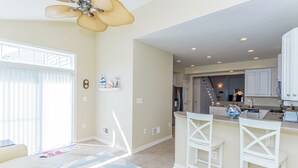 A spacious living area with a large window, a ceiling fan, and a kitchen with white cabinets and a bar area. - Minutes from Fenwick Island & North Ocean City Beaches, Pelicans Perch a 3 bed, 2.5 bath Beautiful Home with Community Pool & Free WIFI (Selbyville)