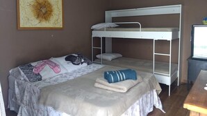 Ein Schlafraum mit Etagenbetten, einem Bett, einem Kissen, einer Decke und einem gerahmten Bild an der Wand.