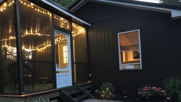 Une maison en bois avec un porche, des guirlandes lumineuses et un petit jardin.