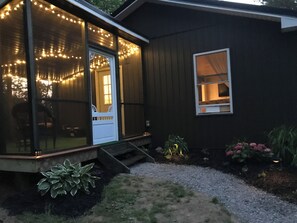 Ett trähus med en veranda, ljusslingor och en liten trädgård.