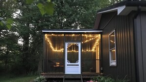 Une petite maison de plain-pied avec une véranda décorée de guirlandes lumineuses.