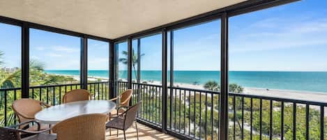 A balcony with a table and chairs, large windows, and a view of the beach.