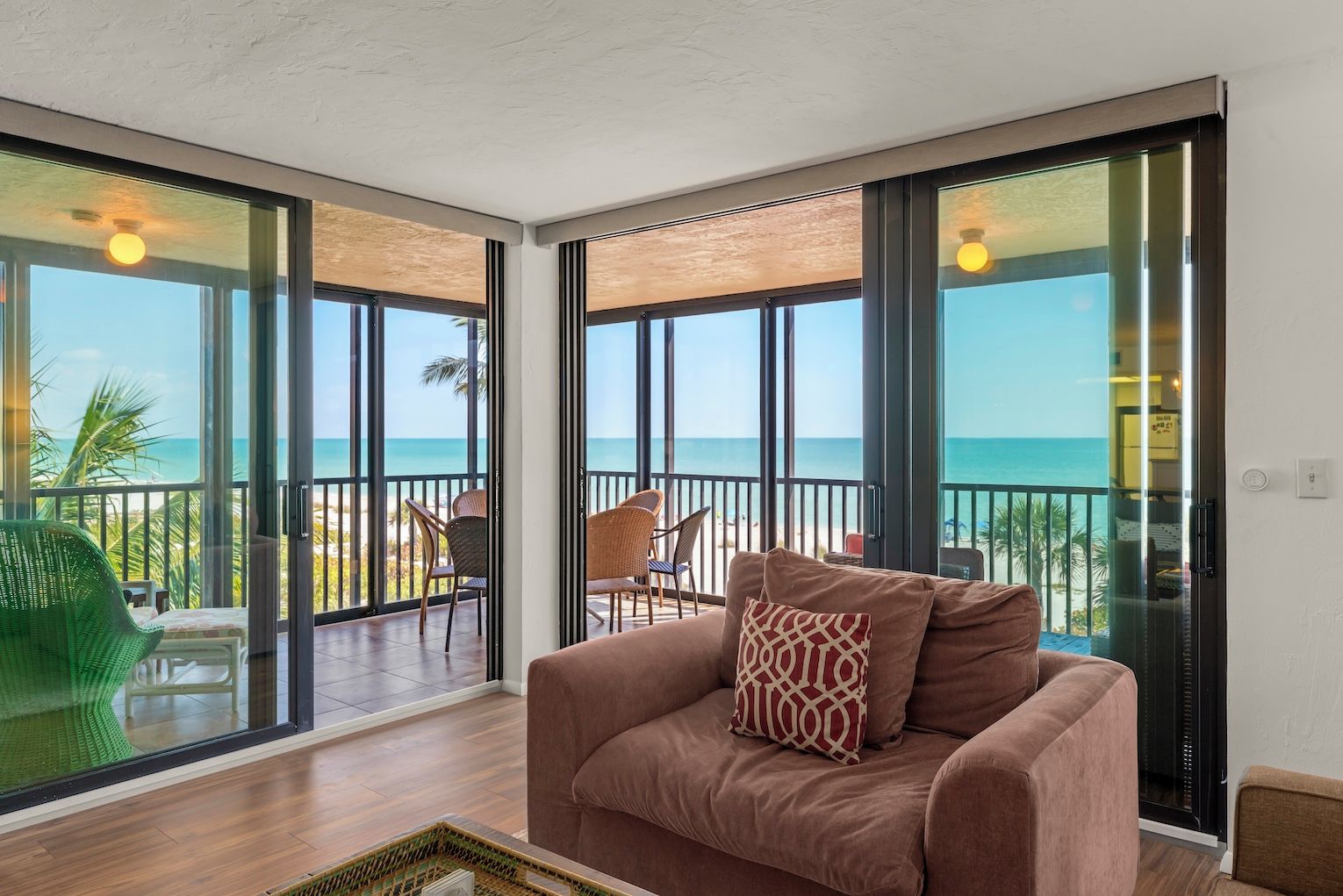 A room with a large sliding glass door leading to a balcony with a view of the beach.