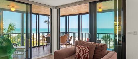 A room with a large sliding glass door leading to a balcony with a view of the beach.