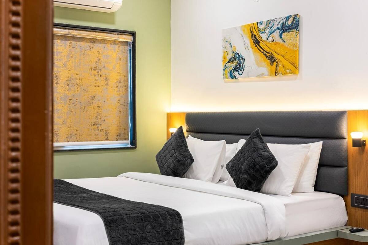 A hotel room with a bed, a painting on the wall, and a window with a curtain.