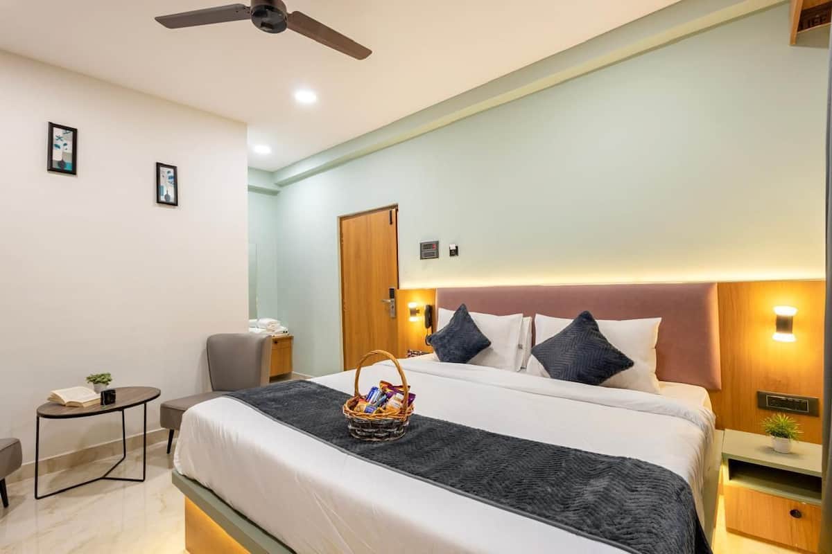 A hotel room with a bed, bedside table, nightstand, ceiling fan, and a wall-mounted light fixture.