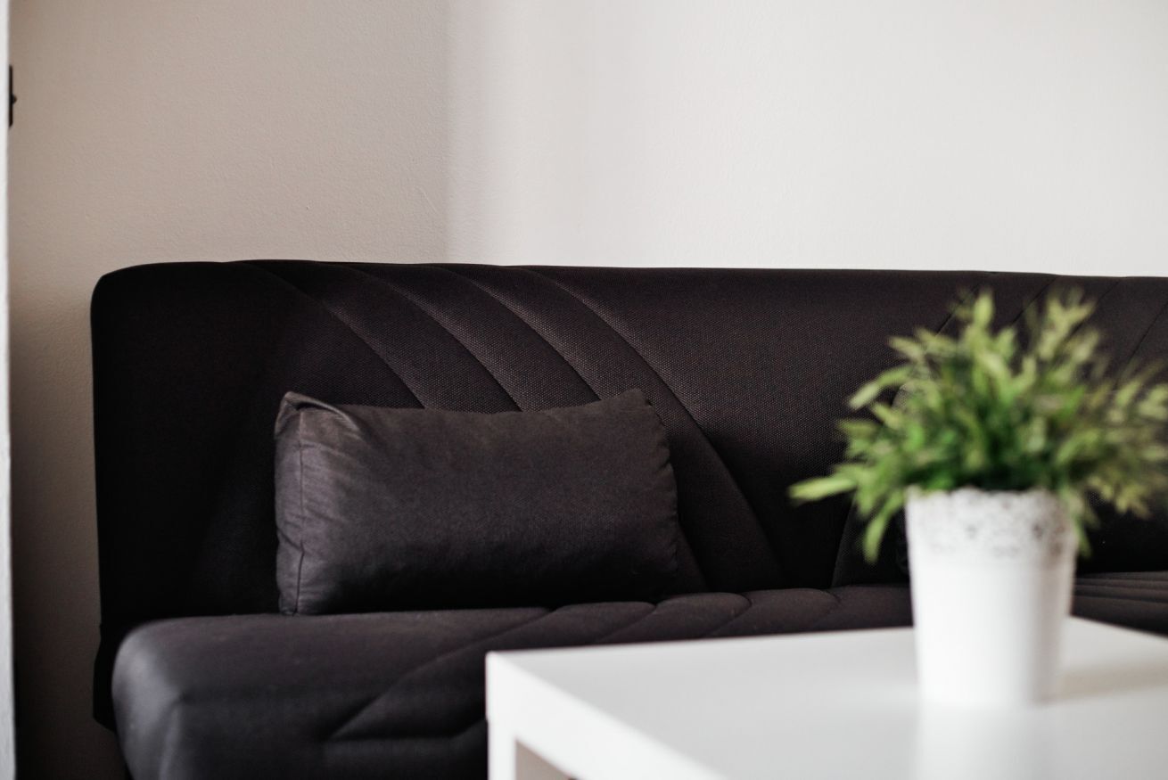 A black sofa with a single cushion, a white table, and a potted plant.