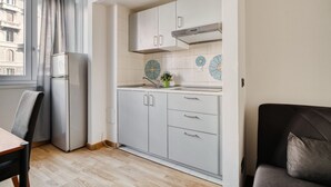 Eine kleine Küche mit Kühlschrank, Schränken und einem Fenster mit Vorhängen.