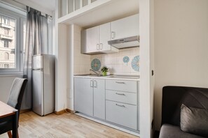Eine kleine Küche mit Kühlschrank, Schränken und einem Fenster mit Vorhängen.