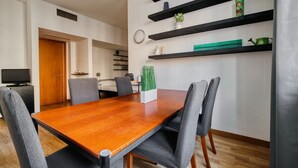 Ein moderner Essbereich mit einem Holztisch, grau gepolsterten Stühlen und schwarzen Regalen mit Dekoration.