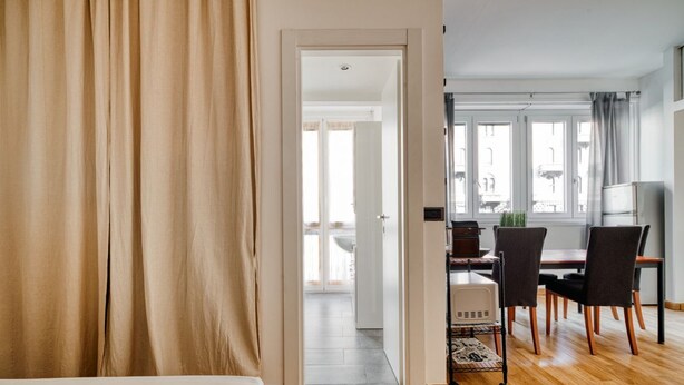 Ein Hotelzimmer mit Bett, einer Essecke mit Stühlen und Tisch sowie Blick durch eine offene Tür.