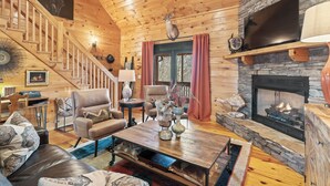 A cozy log cabin interior with a fireplace, wooden staircase, comfortable seating, and a television. - Welcome to Pine and Buck Lodge, a perfect 3 bedroom 2.5 bathroom get away (Ellijay)