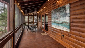 A wooden deck with a table and chairs, a painting on the wall, and a view of the outdoors. - Welcome to Pine and Buck Lodge, a perfect 3 bedroom 2.5 bathroom get away (Ellijay)