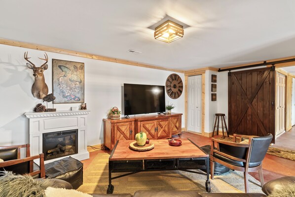 A cozy living room with a fireplace, a television, and a rustic wooden cabinet. - Welcome to Pine and Buck Lodge, a perfect 3 bedroom 2.5 bathroom get away (Ellijay)