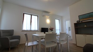 Ein modernes Wohnzimmer mit einem weißen Sofa, einem Esstisch mit Stühlen, einem Flachbildfernseher und einem Bücherregal.