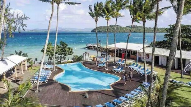 Ein Resort mit Schwimmbad, Liegestühlen und Palmen, mit Blick auf einen Strand und das Meer.