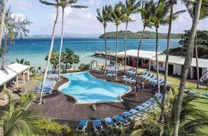 Un resort con piscina rodeada de sillas de descanso y palmeras, con vista a una playa y al océano.