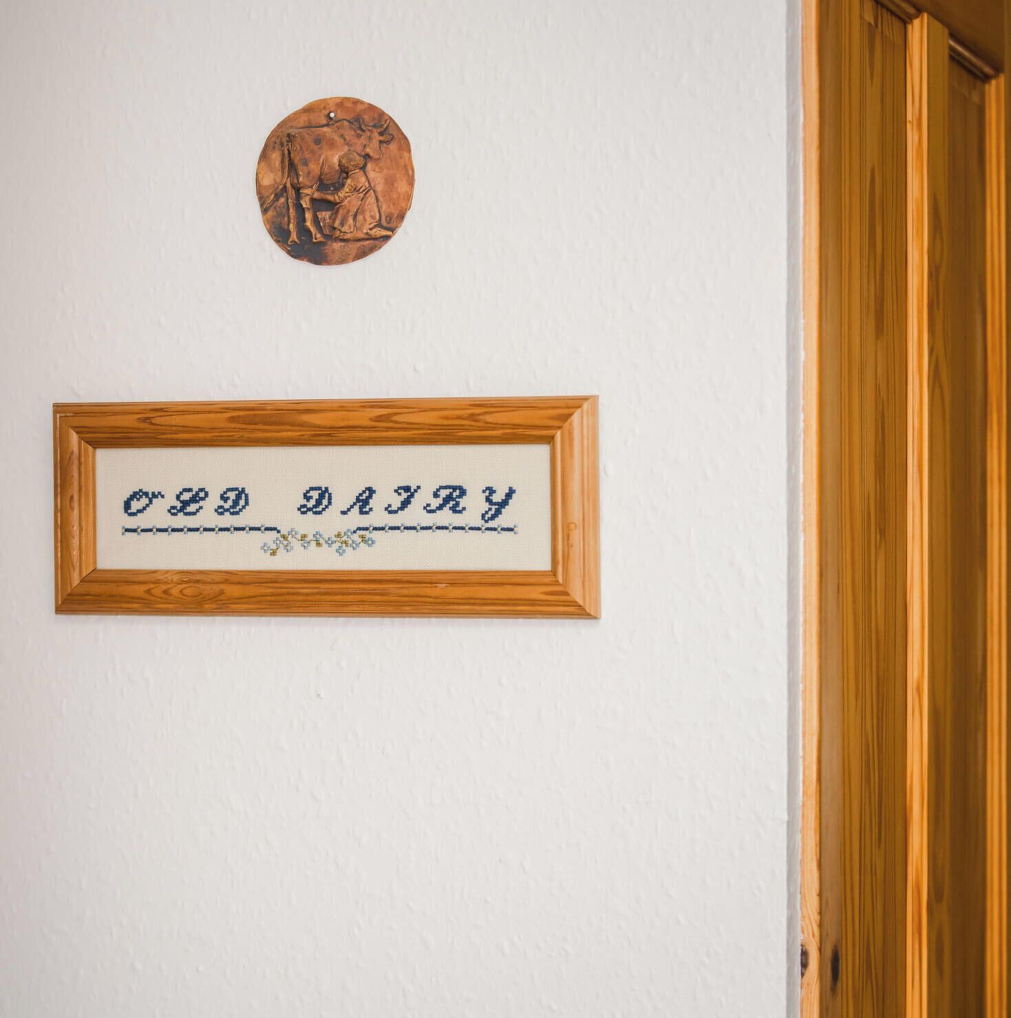 Una obra de arte bordada a mano con hilo, enmarcada, con el texto “RED DADDY” sobre un fondo blanco, colgada en una pared encima de una puerta de madera.