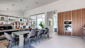 Cocina moderna con comedor, que incluye una isla central, sillas grises y diversos objetos decorativos en estantes.