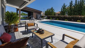Un área junto a la piscina con sillas de descanso, una mesa y un espacio de estar con cojines.