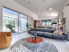 Ein modernes Wohnzimmer mit einem grauen Sofa, einem runden Couchtisch und einem großen Fenster.