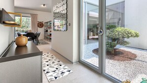 Un interior moderno con zona de comedor, un pasillo que conduce a una puerta corrediza de vidrio y un pequeño jardín visible a través de la puerta.