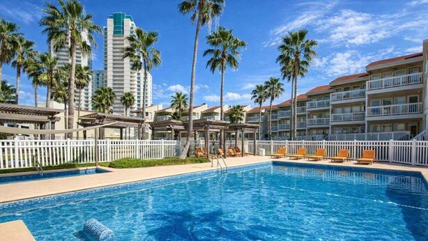 Una piscina alberghiera con acqua cristallina, circondata da palme e un recinto bianco.