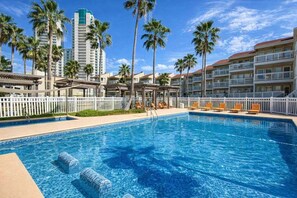 Una piscina de hotel con agua cristalina azul, rodeada de palmeras y una cerca blanca.